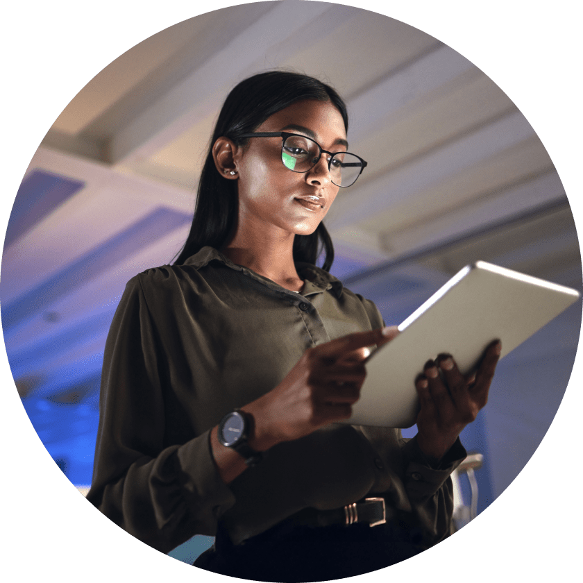 Eine Frau mit Brille, die ein Tablet in der Hand hält, während sie in einem gut beleuchteten Innenraum steht. Sie hat langes schwarzes Haar und trägt eine dunkle Bluse. Die Umgebung ist in dezentes blaues Licht getaucht.