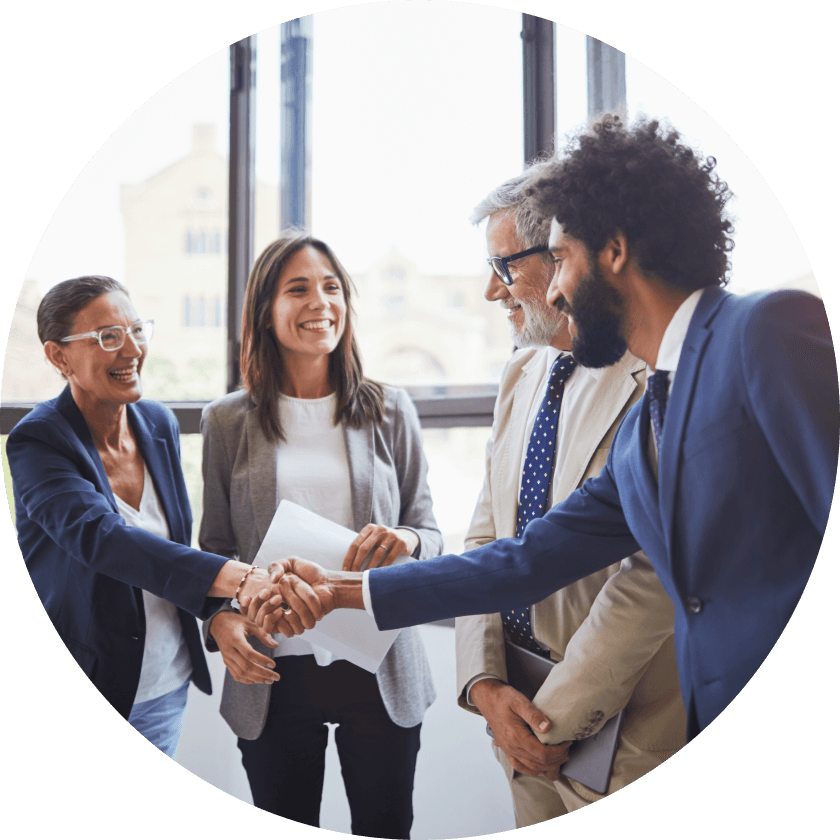 Eine Gruppe von vier Fachleuten, zwei Frauen und zwei Männer, die sich in einem Büro mit großen Fenstern im Hintergrund die Hände reichen. Sie sind in Business-Kleidung gekleidet und scheinen in ein positives Gespräch vertieft zu sein.