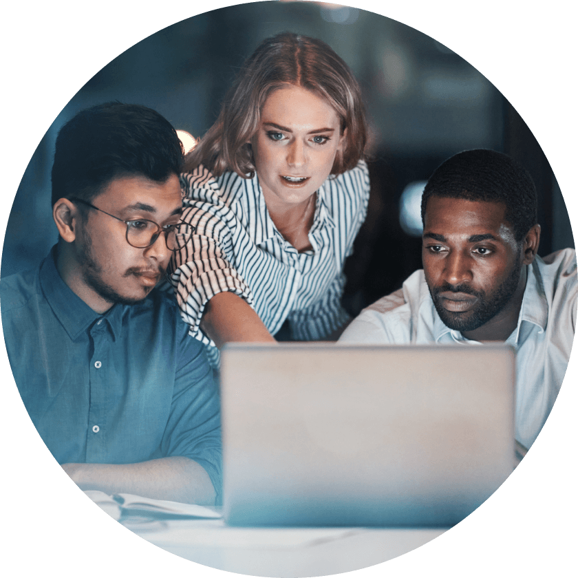 Drei Kollegen unterhielten sich, während sie in einer schwach beleuchteten Umgebung auf einen Laptop-Bildschirm schauten.