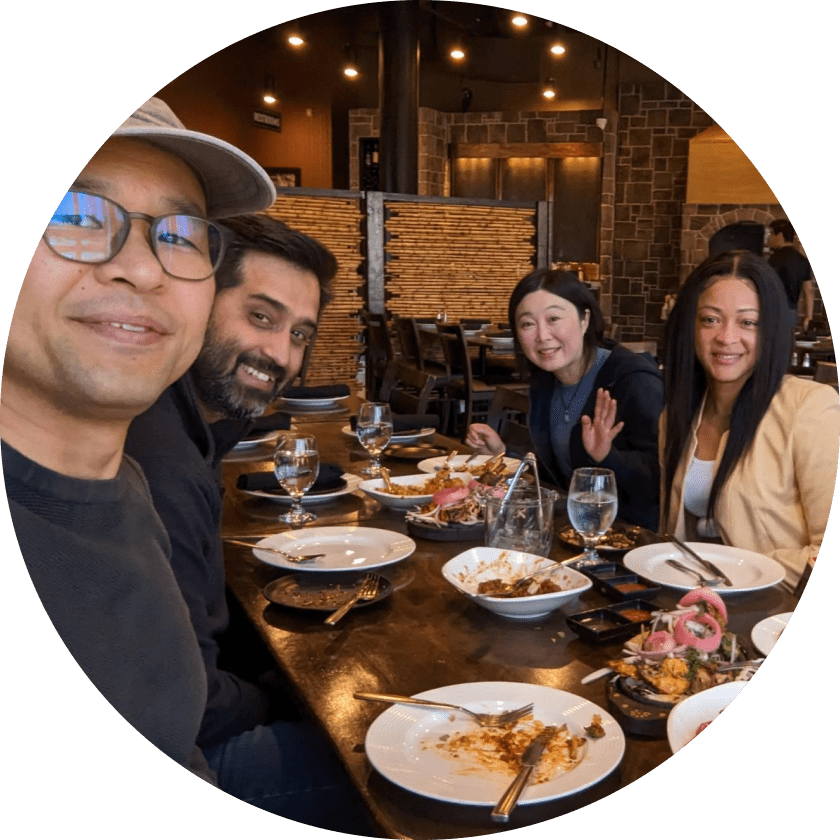 Vier Personen sitzen an einem Tisch in einem Restaurant, lächeln und posieren für die Kamera. Der Tisch ist mit leeren Tellern und Gläsern gedeckt, was darauf hindeutet, dass sie ihre Mahlzeit beendet haben. Das Restaurant hat eine warme Atmosphäre mit Holzdekor.