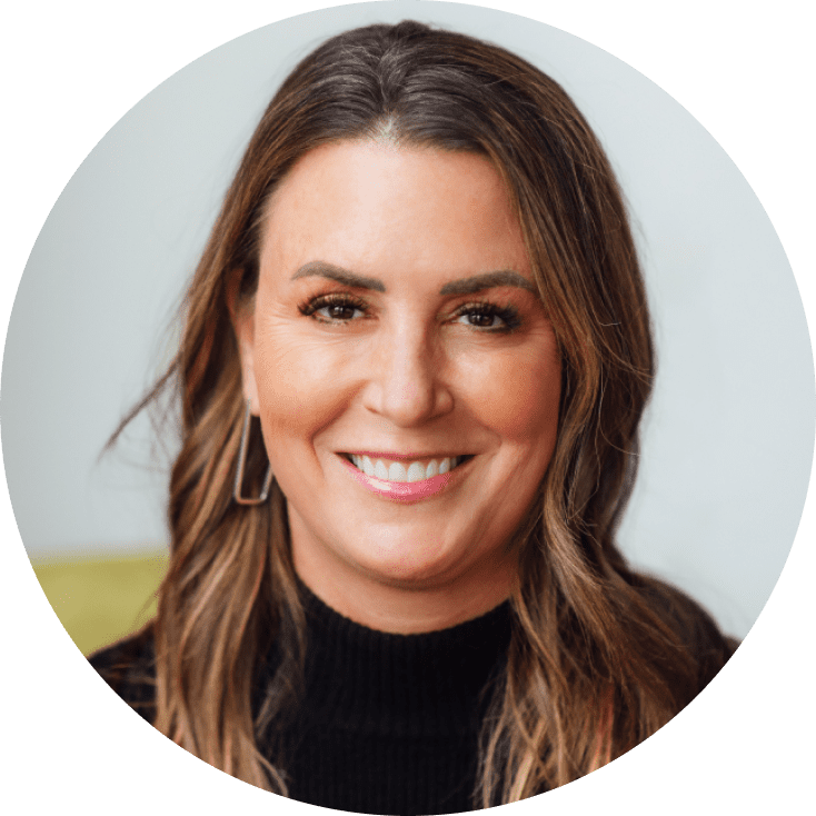 Ein Nahaufnahme-Porträt einer Frau mit langen braunen Haaren, die warm lächelt und einen schwarzen Rollkragenpullover trägt. Der Hintergrund ist weich und hell in der Farbe, die eine freundliche Atmosphäre schafft.