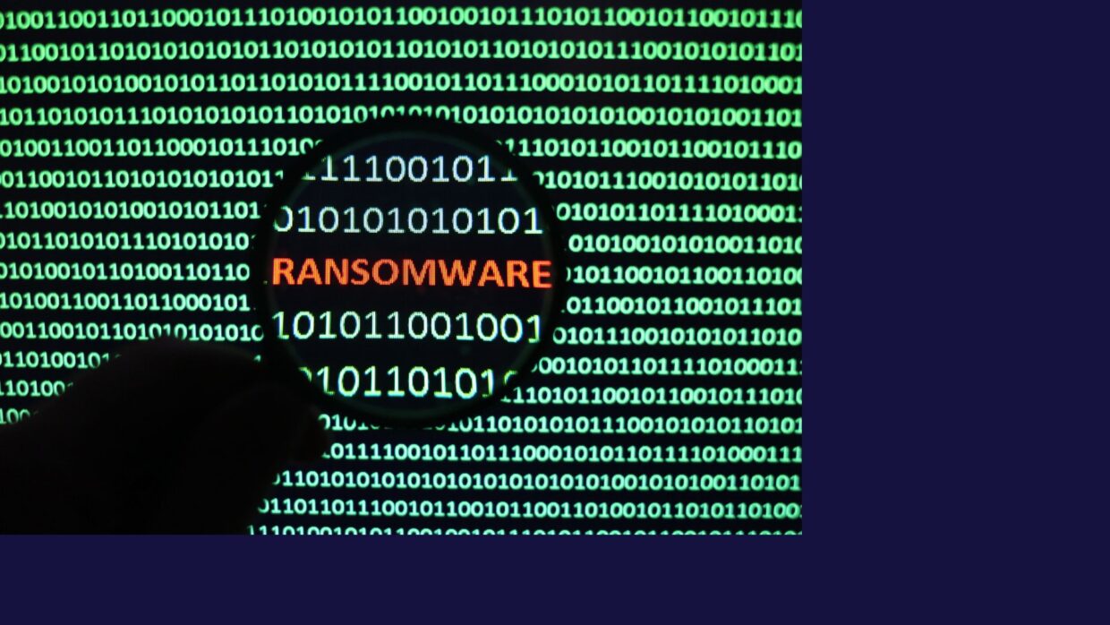 Nahaufnahme eines Binärcodes auf einem digitalen Bildschirm, wobei das Wort 'RANSOMWARE' durch eine Lupe in Orange hervorgehoben wird. Dieses Bild veranschaulicht das Konzept der Ransomware in der digitalen Sicherheit.