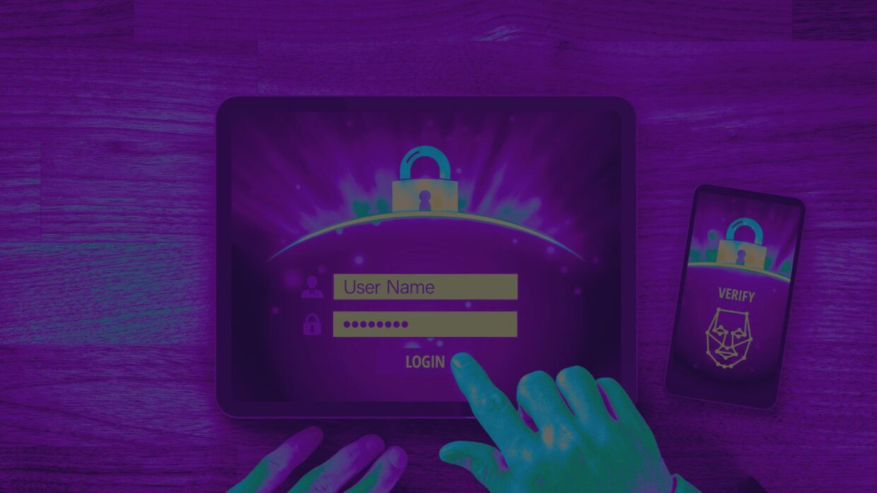 Eine Person, die ihre Anmeldedaten über ein Touchscreen-Tablet eingibt, mit einem Schloss-Symbol auf dem Bildschirm. Daneben liegt ein Smartphone, auf dem eine Bestätigungsaufforderung angezeigt wird. Dies veranschaulicht, wie Cyberkriminelle integrierte Microsoft-Tools ausnutzen.