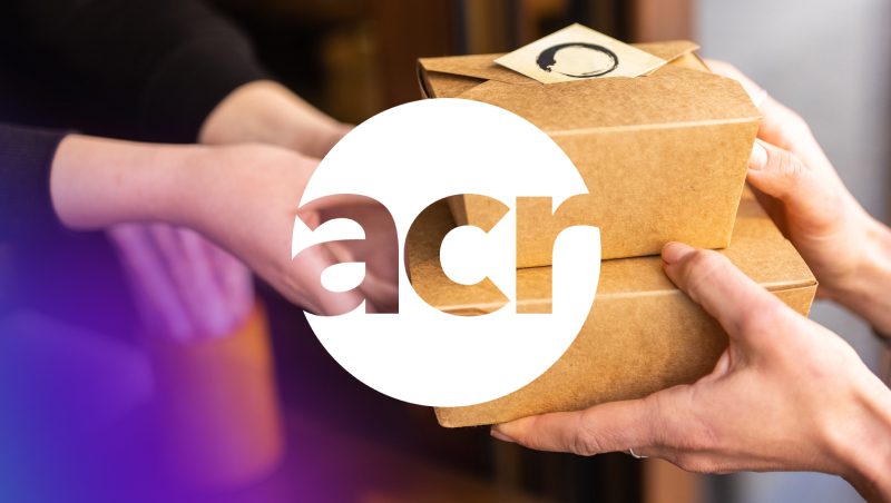 Ein Paar Hände, die zwei braune Imbissschachteln austauschen, mit einem Logo-Overlay, das die Buchstaben 'acr' enthält. Der Hintergrund hat einen weichen Übergang von Lila zu Weiß.