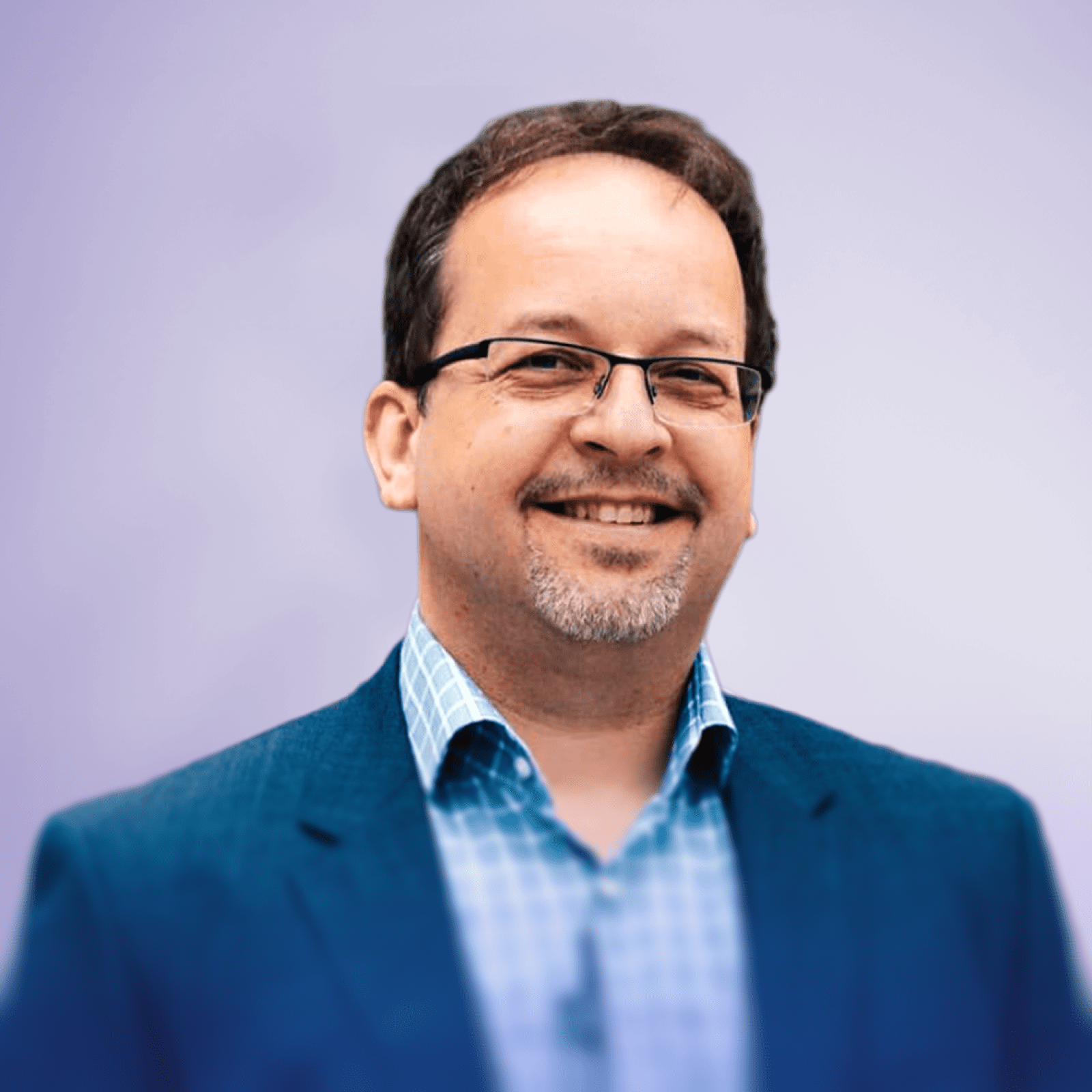Andreas Seidl, der einen dunklen Blazer über einem karierten Hemd trägt, steht im Freien vor einem weichgezeichneten Hintergrund aus Grünpflanzen.