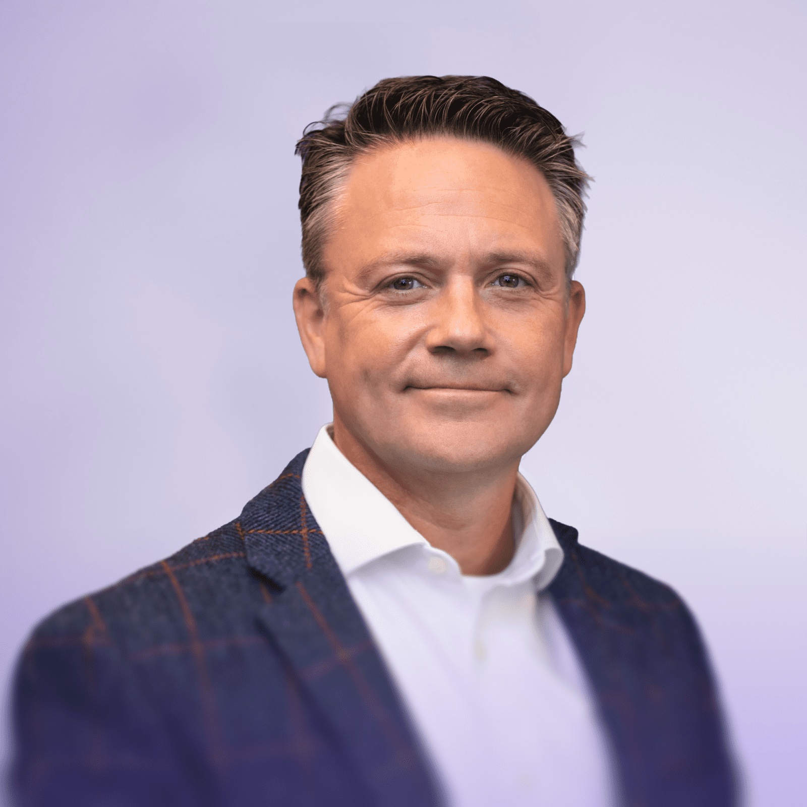 Ein professionelles Kopffoto eines lächelnden Mannes. Er hat kurzes dunkles Haar und trägt einen braunen, karierten Blazer über einem weißen Hemd. Der Hintergrund ist einfarbig weiß, so dass sein Gesicht klar und deutlich zu erkennen ist.