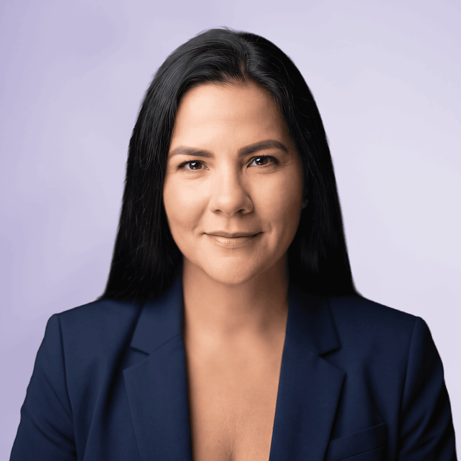 Eine Frau mit langen dunklen Haaren trägt einen marineblauen Blazer vor einem hellvioletten Hintergrund.